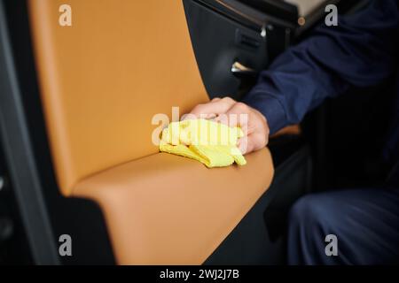 vue rognée d'un spécialiste dévoué travaillant dur dans la voiture de nettoyage uniforme bleu avec chiffon jaune Banque D'Images