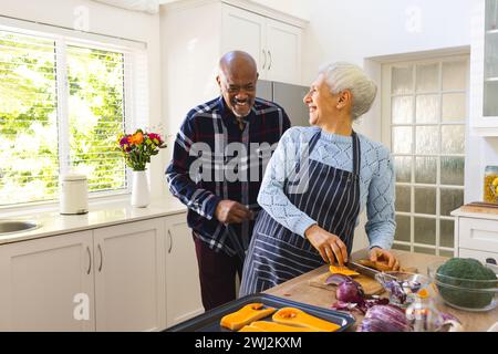 Heureux couple senior diversifié hachant des légumes dans la cuisine Banque D'Images