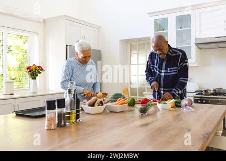 Couple senior diversifié hachant des légumes dans la cuisine Banque D'Images