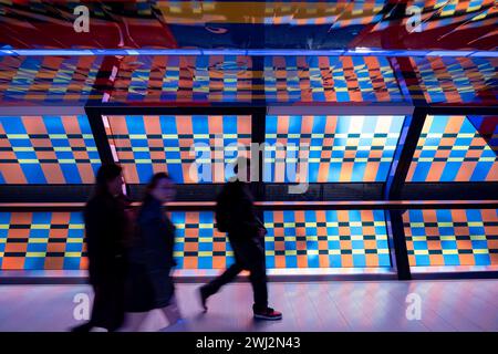 Des personnes interagissant avec l’œuvre d’art contemporain publique géométrique captivée par Colour par l’artiste Camille Walala dans la passerelle du tunnel à Adams Plaza Bridge reliant North Collonade à Crossrail place au cœur du quartier financier de Canary Wharf le 6 février 2024 à Londres, Royaume-Uni. Canary Wharf est une zone située près de l'île des chiens dans le quartier londonien de Tower Hamlets et est définie par la Greater London Authority comme faisant partie du quartier central des affaires de Londres. Banque D'Images