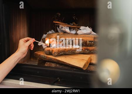 Main femelle tient une allumette, prête à enflammer le bois de chauffage dans une cheminée Banque D'Images