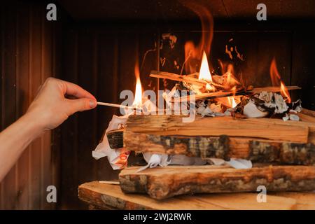 Main femelle tient une allumette, prête à enflammer le bois de chauffage dans une cheminée Banque D'Images