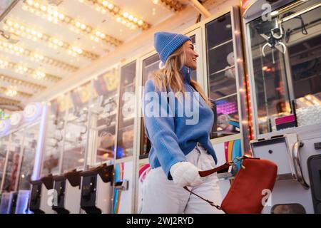 Femme joyeuse et élégante, vêtue de vêtements chauds, s'amuse dans un parc d'attractions hivernal enneigé Banque D'Images