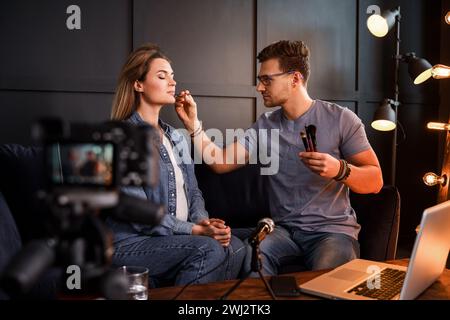 Jeune blogueur masculin de beauté applique le maquillage à la belle jeune femme Banque D'Images