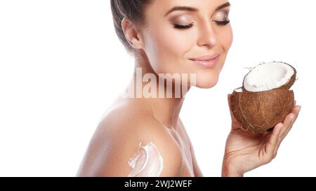 Belle femme appliquant de la crème sur son corps à base d'huile de noix de coco sur fond blanc Banque D'Images