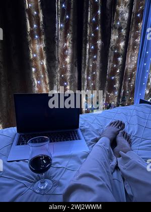 Un verre de vin, un ordinateur portable sur le lit. Banque D'Images