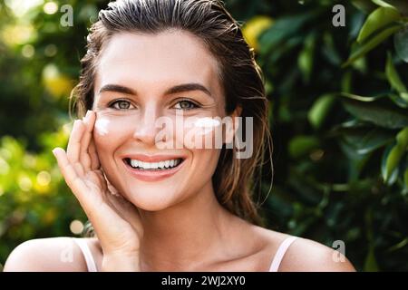 Belle femme avec de la crème hydratante sous ses yeux Banque D'Images