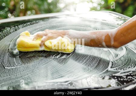 Main féminine avec éponge jaune lavant le pare-brise de la voiture Banque D'Images