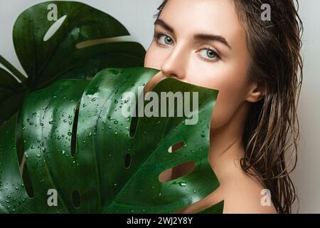 Jeune femme avec une peau lisse tenant la feuille de plante Monstera deliciosa Banque D'Images