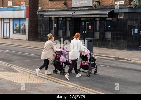 Deux femmes poussant des landaus, traversent une route vers un pub à Hull, East Yorkshire. Banque D'Images