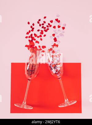 Disposition créative d'amour faite avec des lèvres rouges et des confettis de paillettes en forme de coeur sortant de verres à champagne sur fond rouge et rose. Concept minimal. Banque D'Images