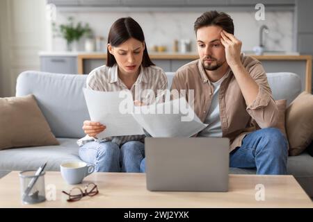Couple anxieux avec ordinateur portable et papiers sur le canapé Banque D'Images