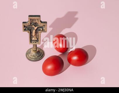 Mise en page créative faite avec Christian Holy Cross et des œufs de Pâques de couleur rouge sur fond rose clair. Concept minimal de Pâques. Banque D'Images