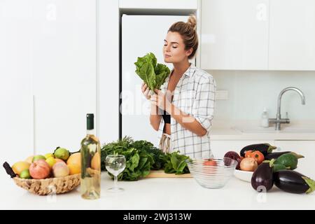 Jeune jolie femme avec des feuilles de laitue reniflées pendant la cuisson Banque D'Images