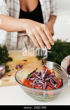 Mains femelles cuisiner une salade végétarienne et y ajouter de l'oignon rouge Banque D'Images