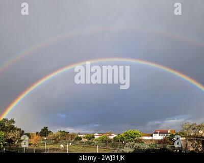 Un grand double arc-en-ciel au-dessus d'un champ agricole. Deux arches colorées dans le ciel sombre nuageux dans la campagne au Portugal. Photo horizontale Banque D'Images