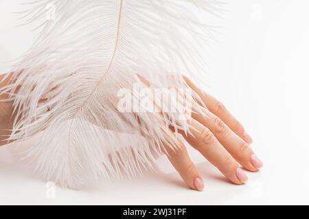Main féminine avec peau lisse et plume d'autruche douce sur fond blanc Banque D'Images