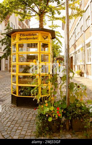 Cabine téléphonique allemande traditionnelle avec fleurs. Ancienne cabine téléphonique jaune en Allemagne avec texte Ã¶ffen Banque D'Images