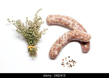 Saucisses de porc bratwurst crues allemandes sur blanc avec un bouquet de thym et poivre multicolore - Seasonin Banque D'Images