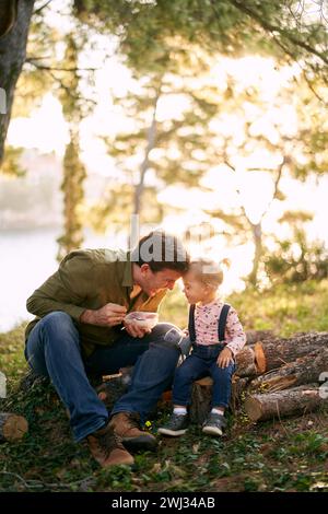 Papa pencha son front contre le front d'une petite fille assise avec elle sur des bûches dans la forêt Banque D'Images