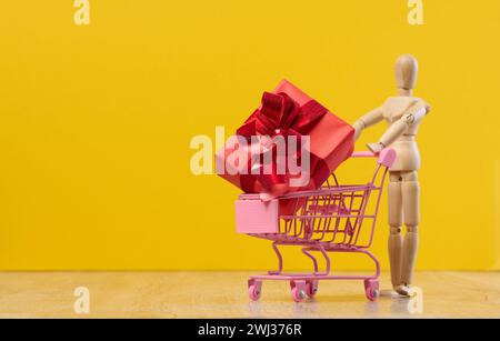 Cadeau dans un panier miniature et mannequin en bois sur fond jaune Banque D'Images