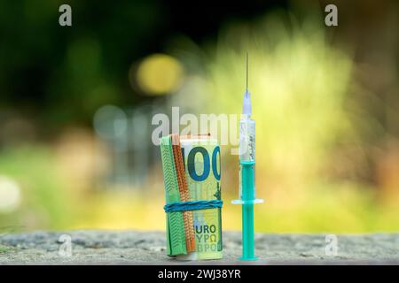 Seringue et Euro Money roll. Billets de 100 et 50 euros torsadés en tube et attachés avec une bande élastique. Banque D'Images