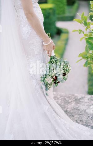 Mariée avec un bouquet se tient à moitié tourné dans le parc. Vue latérale. Rogné Banque D'Images