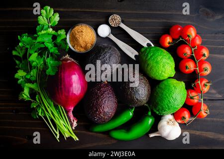 Ingrédients frais de guacamole sur une table en bois rustique : avocats Haas, citrons verts, coriandre et autres ingrédients pour la trempette de guacamole sur un fond sombre Banque D'Images