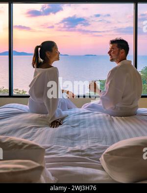 Couple homme et femme devant le lit dans la chambre pendant le lever du soleil buvant une tasse de café Banque D'Images