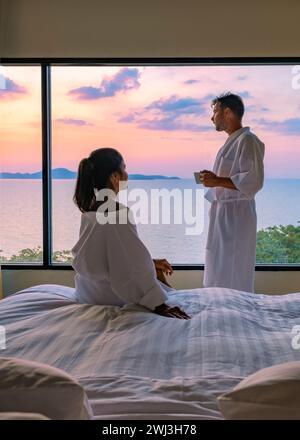 Couple homme et femme devant le lit dans la chambre pendant le lever du soleil buvant une tasse de café Banque D'Images