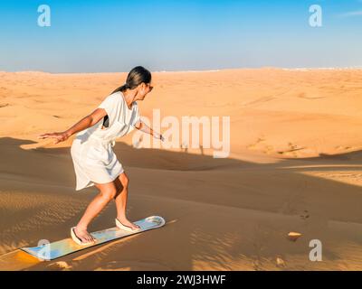 Jeunes femmes surfant sur le sable dans les dunes de sable de Dubaï Émirats Arabes Unis Banque D'Images