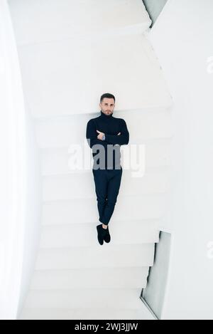 Homme en tenue noire couché sur un escalier blanc Banque D'Images