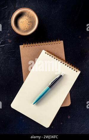 Maquette de cahier avec un stylo et une tasse de café, top shot sur noir Banque D'Images