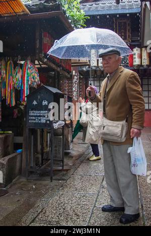 Ancien homme japonais avec parapluie sur Shijo Dori Street dans le centre-ville de Gion, Kyoto, Japon sous la pluie. Banque D'Images