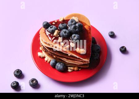 Assiette avec de savoureuses crêpes en forme de coeur, myrtille et confiture sur fond violet. Célébration de la Saint-Valentin Banque D'Images