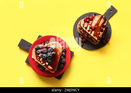 Planches d'ardoise avec de savoureuses crêpes en forme de coeur et de baies sur fond jaune. Célébration de la Saint-Valentin Banque D'Images