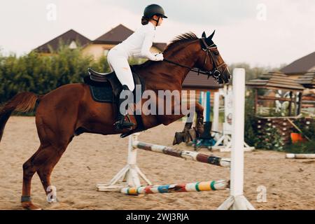 Vue latérale de la barrière de saut de cheval de dressage avec jockey de cavalier féminin en uniforme blanc pendant la compétition de saut. Banque D'Images