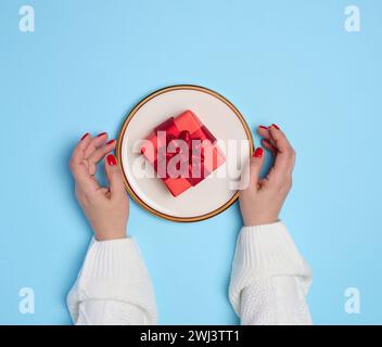 Deux mains féminines tenant une assiette avec un cadeau sur fond bleu Banque D'Images
