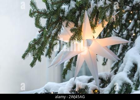 Étoile morave blanche illuminée (Herrnhuter Stern allemand) suspendue dans un sapin de Noël recouvert de neige comme décoration de fête Banque D'Images