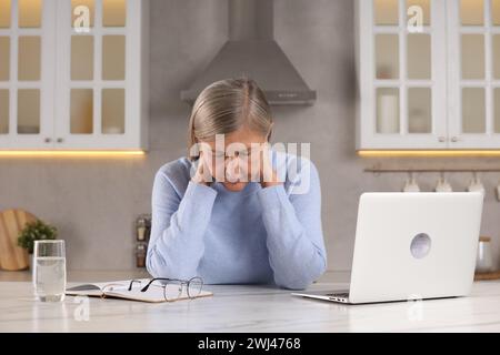 Ménopause. Femme souffrant de douleur dans le cou à table dans la cuisine Banque D'Images