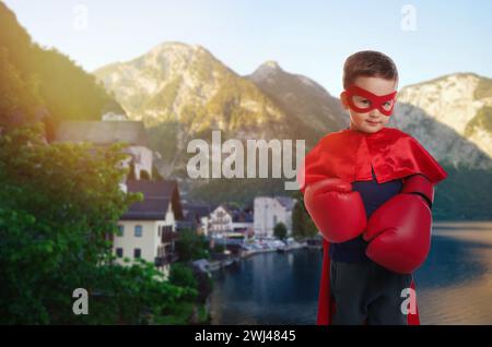 Super-héros, motivation et puissance. Garçon en cape et masque portant des gants de boxe dans les montagnes Banque D'Images