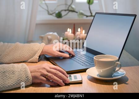 Achats en ligne pour les vacances sur un budget, mains d'une femme plus âgée à l'aide d'un ordinateur portable et d'une calculatrice, table avec des bougies de l'AVENT, Christ Banque D'Images