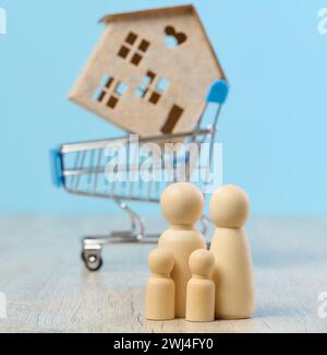 Maison en bois et figurines miniatures d'une famille sur fond bleu. Le concept de vente et d'achat de biens immobiliers Banque D'Images
