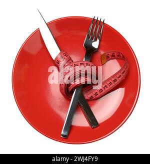 Assiette ronde rouge et fourchette et couteau enveloppés dans un ruban à mesurer vert Banque D'Images