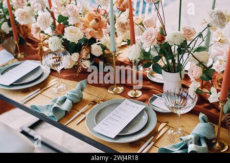 Des bouquets de fleurs se dressent sur la table à côté du menu festif sur des assiettes Banque D'Images