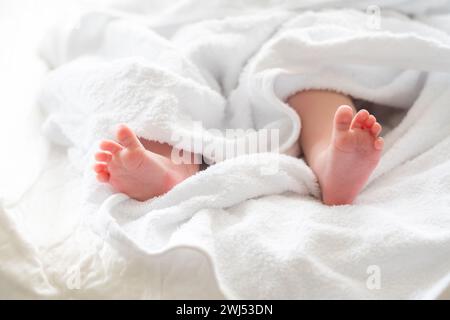 De minuscules pieds nouveau-nés émergent doucement d'une serviette. Concept de sérénité post-bain Banque D'Images