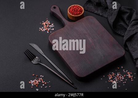 Planche à découper en bois vide avec épices et herbes sur fond de béton foncé Banque D'Images