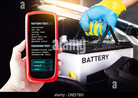 Testeur de batterie dans une main de mécanicien de voiture pour tester la tension de batterie et la santé de batterie, concept de service d'entretien de voiture Banque D'Images