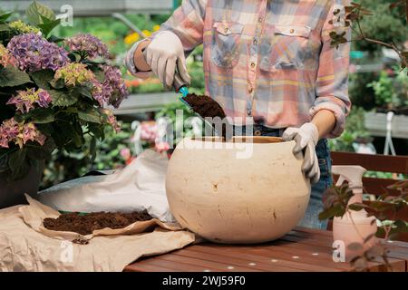 Femme plantant la fleur dans le pot en utilisant la saleté dans le centre de jardin Banque D'Images