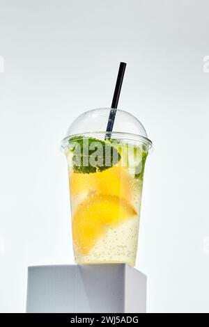 Limonade avec citron, orange, citron vert et menthe dans du verre en plastique transparent sur fond blanc Banque D'Images
